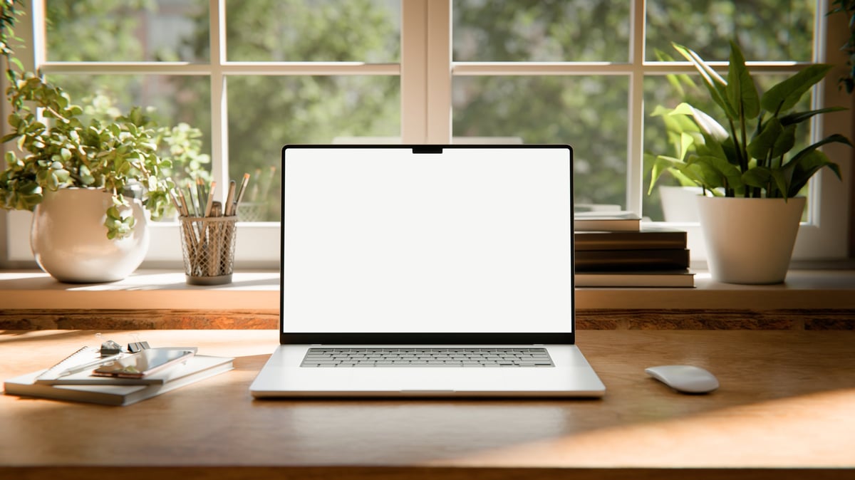 laptop screen mockup images captured in a bright industrial loft interior. Placed on a wooden desk near large windows with natural daylight, exposed brick walls, and green plants, creating a warm and stylish workspace atmosphere.